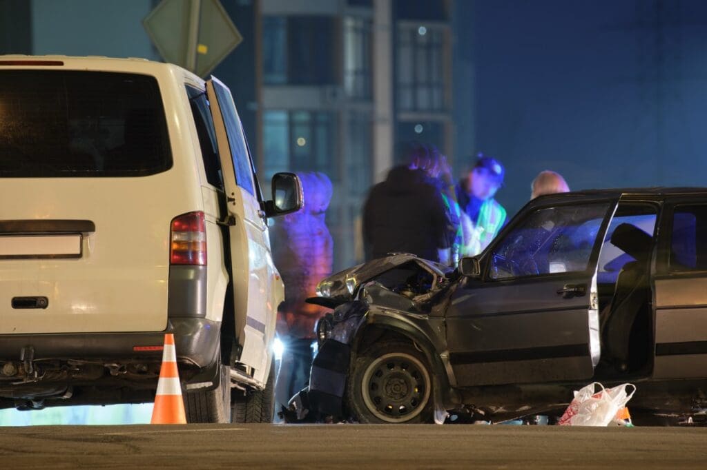 Cars crashed heavily in road accident after collision and silhouette of people on city street at night.