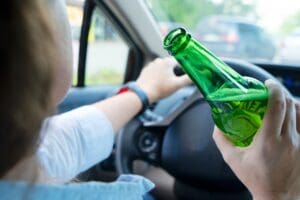 Someone driving and holding a bottle with alcohol. Drunk driving concept