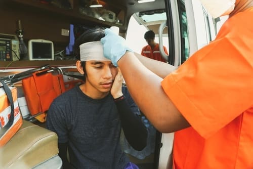 A paramedic in orange scrubs treats a young man with a head injury inside an ambulance.