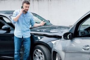 Charlotte Hit and Run Accident Lawyer - Payne Law Firm A man stands next to two cars involved in an accident, talking on his phone and gesturing toward the damaged vehicles.