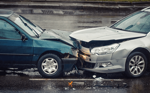 Two cars involved in a front-end collision on a wet road, with visible damage to the front of both vehicles.