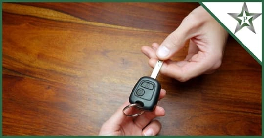 A person hands over a car key with a remote, above a wooden surface.