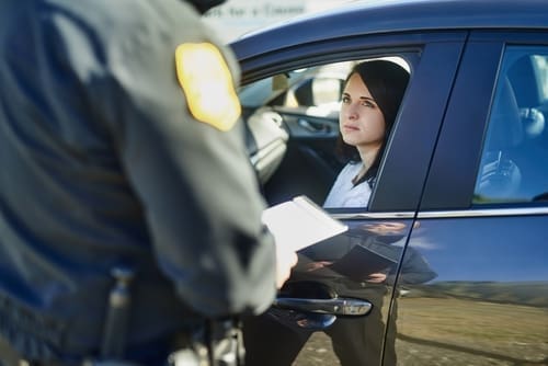 A police officer stands beside a car and speaks with a woman sitting in the driver's seat during a traffic stop.