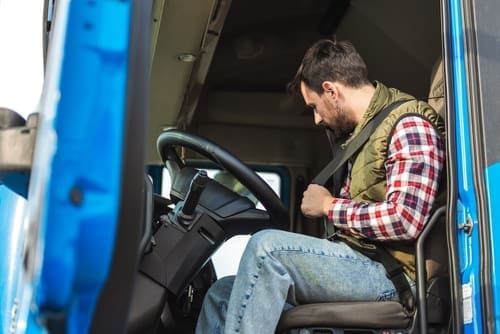 Young truck driver fastening seat belt inside commercial vehicle cab