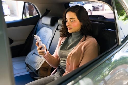 Female passenger using smartphone while seated in rideshare vehicle back seat