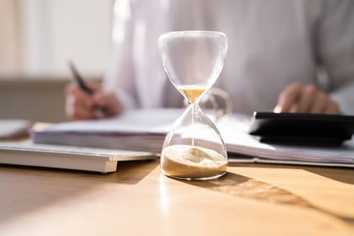 hourglass on desk with person reviewing documents and using calculator