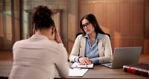 female attorney in glasses listening to distressed client across office desk