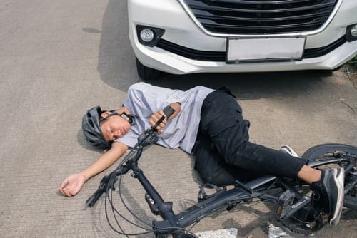 injured cyclist lying on road beside fallen bicycle after vehicle collision