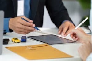 Charlotte Hit and Run Accident Lawyer - Payne Law Firm Two people review a digital contract on a tablet at a desk with toy cars, a pen, keys, and a yellow envelope.