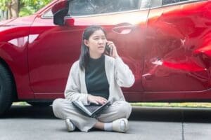 Charlotte Hit and Run Accident Lawyer - Payne Law Firm woman sitting on ground calling for help beside dented damaged car