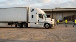 semi-truck parked at warehouse loading dock with workers wearing safety vests