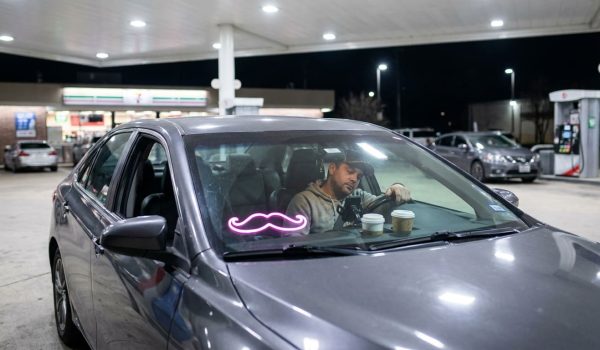 Lyft driver looking at phone in parked car at gas station