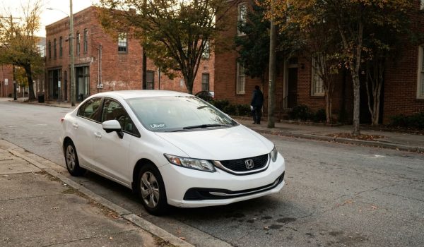 Honda sedan with Uber decal parked on urban street near brick buildings
